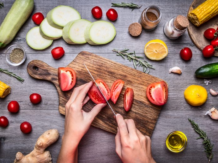 Female hand cut tomatoes rustic kitchen table,vegetarian concept.